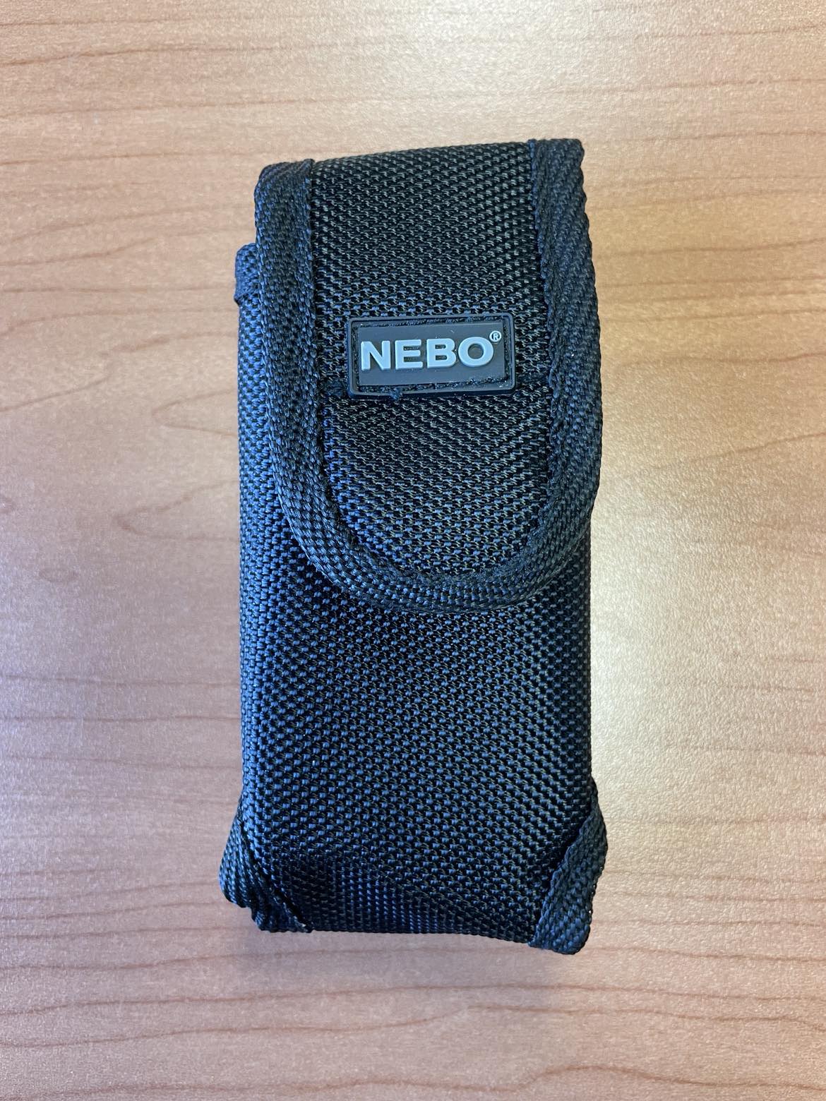 The Nebo 6274 Flashlight Holster is made of black durable nylon with the name a third of the way down.