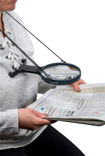 A woman is using the around the neck magnifier to read a newspaper.